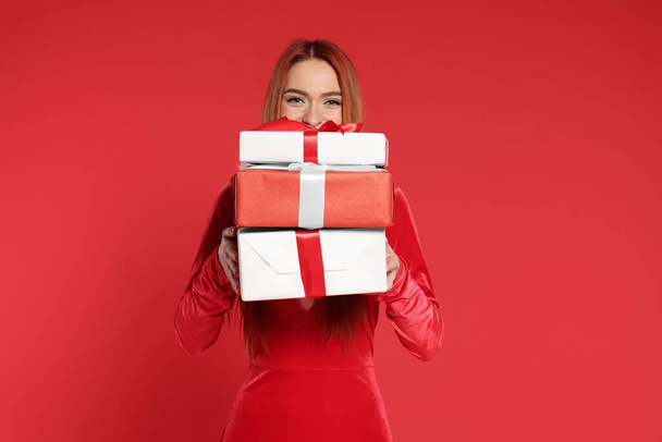 Young woman with Christmas gifts on red background - Фото, изображение