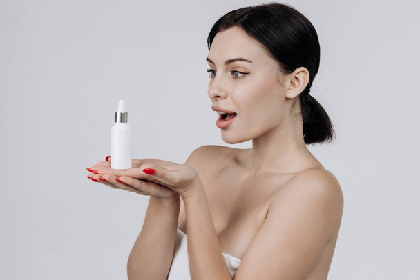 Closeup beautiful woman with perfect natural skin hold mockup tube face serum for skincare treatment product advertising expressive facial and gesture expression in isolated background. - Foto, Imagen