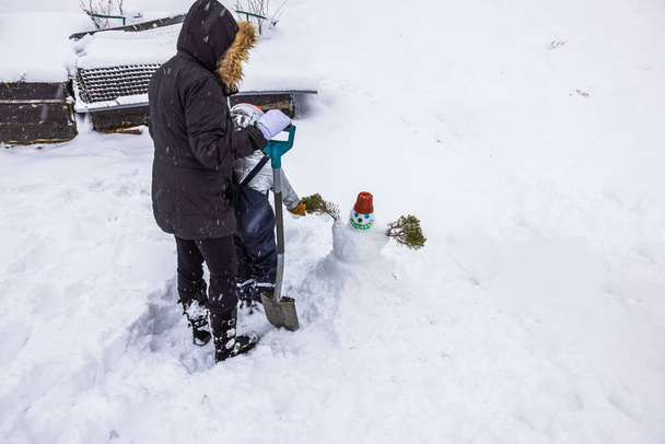 Näkymä naisen ja lapsen iloisesti veistämällä pieni lumiukko yhdessä takapihallaan. Ruotsi. - Valokuva, kuva