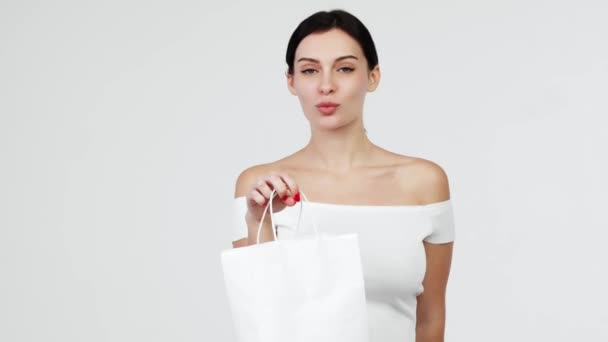 Dívka snila o nakupování. Usmívající se elegantní žena představuje papírové nákupní tašky, izolované na bílém pozadí.  - Záběry, video