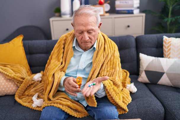 Moyen âge homme aux cheveux gris prenant des pilules assis sur le canapé à la maison - Photo, image