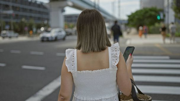 美しいヒスパニックの女性が眼鏡をかけ,気軽に歩き去り,東京の現代的な通り沿いの携帯電話で,彼女の背中の景色を示しています. - 写真・画像