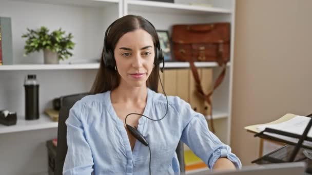 Mujer hispana joven, fresca y confiada con una hermosa sonrisa, orgullosamente usando auriculares en la oficina, irradia un estilo de vida positivo y éxito - Metraje, vídeo