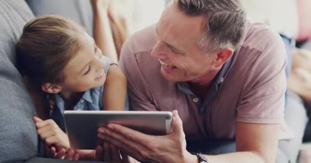 Digital tablet, relax and child with her father browsing on social media or mobile app at home. Happy, smile and dad scrolling on the internet with his girl kid while laying on a sofa in living room - Footage, Video