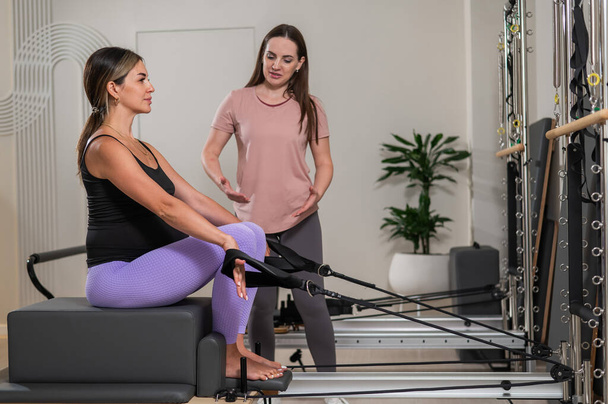 Caucasian pregnant woman doing Pilates exercises on a reformer machine with an individual trainer - Fotoğraf, Görsel