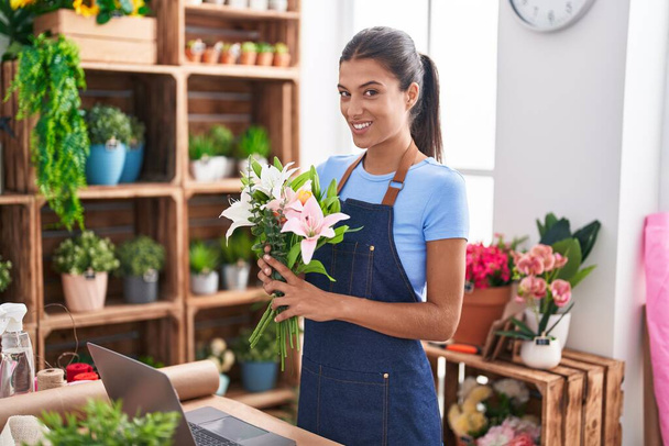 Young beautiful hispanic woman florist holding bouquet of flowers at florist - Photo, Image