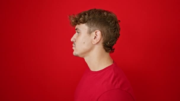Joven hombre hispano de pie con expresión seria sobre fondo rojo aislado - Imágenes, Vídeo
