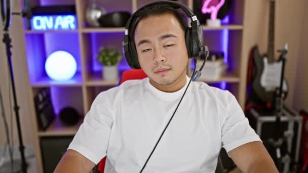 Homem chinês jovem confiante, um streamer gamer digital, sorrindo com fone de ouvido na sala de jogos escura, dominando entretenimento cibernético futurista enquanto streaming - Filmagem, Vídeo