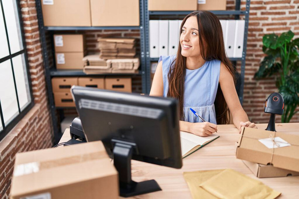 Молодая красивая латиноамериканка в электронной коммерции бизнес-работница с помощью компьютера записи на ноутбуке в офисе - Фото, изображение