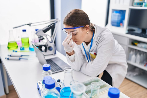 Young caucasian woman scientist stressed using laptop at laboratory - Photo, image