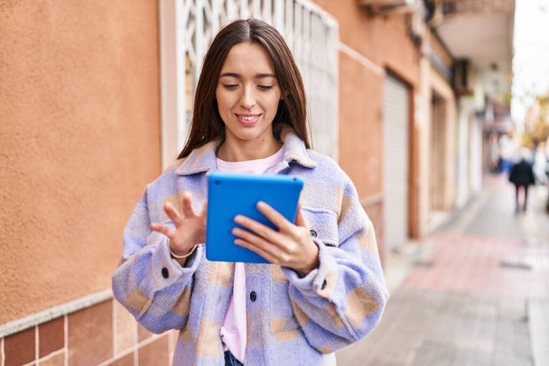 Joven hermosa mujer hispana sonriendo confiada usando touchpad en la calle - Foto, Imagen