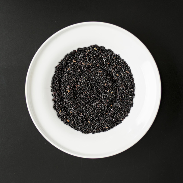Black rice heap in ceramic dish top view close up isolated on black background  - Foto, afbeelding