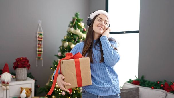 Νεαρή λευκή γυναίκα γιορτάζει τα Χριστούγεννα ακούγοντας μουσική και χορεύοντας στο σπίτι - Φωτογραφία, εικόνα