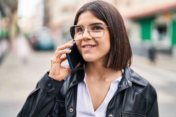 Joven hermosa mujer hispana sonriendo confiada hablando en el teléfono inteligente en la calle - Foto, imagen