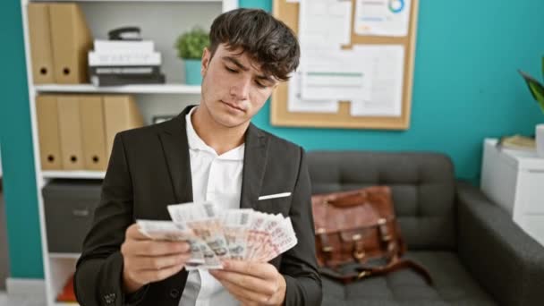 Confident young hispanic teenager working hard in business, counting krona banknotes in the office, displaying wealth in icelandic currency - Footage, Video