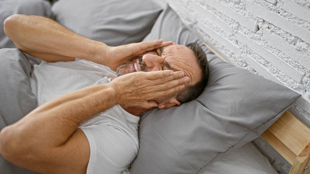 Middle age man with grey hair lying on bed suffering for headache at bedroom - Foto, Imagen