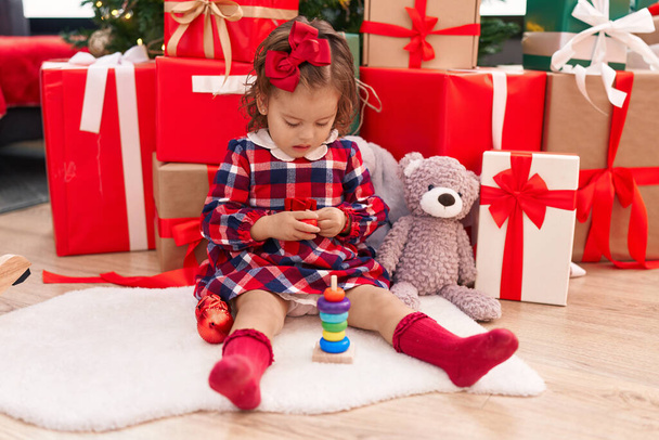 Rozkošné blondýny batole drží hračku sedí u vánočního stromečku doma - Fotografie, Obrázek