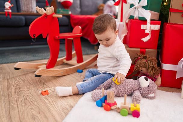 Αξιολάτρευτο καυκάσιο μωρό κάθεται στο πάτωμα με χριστουγεννιάτικα δώρα παίζοντας στο σπίτι - Φωτογραφία, εικόνα