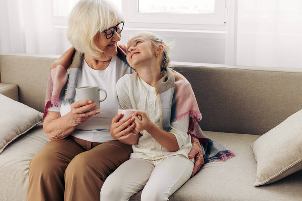 Жінка-бабуся обіймає дівчину зимовий домашній плетений кухоль онука сім'я старий диван літня диван старший літня людина сидить щасливе кохання спосіб життя диван дочка обіймає матір - Фото, зображення