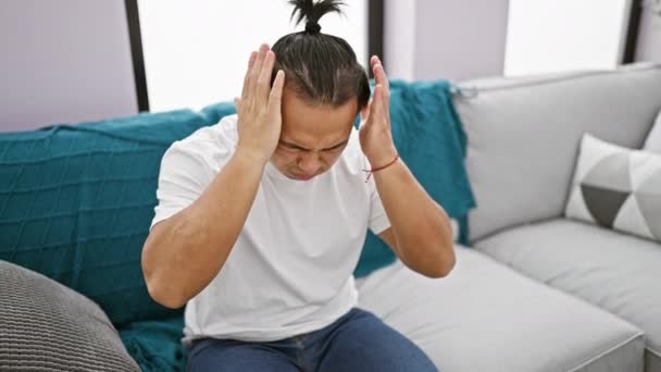 Stresli genç Çinli adam, hayal kırıklığına uğramış ve yalnız, evinde bir baş ağrısı ve kişisel anlaşmazlık içinde oturuyor. - Video, Çekim