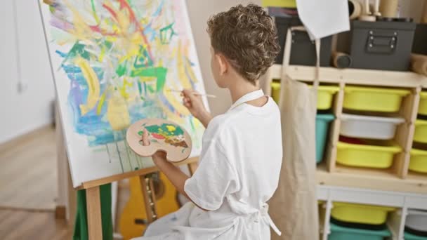 Adorável loiro menino artista, confiantemente sorrindo como ele gosta de desenhar no estúdio de arte, imerso em sua lição de pintura - Filmagem, Vídeo