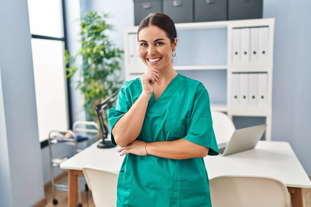 Giovane bella infermiera donna ispanica sorridente fiducioso in piedi con le braccia incrociate gesto alla clinica - Foto, immagini