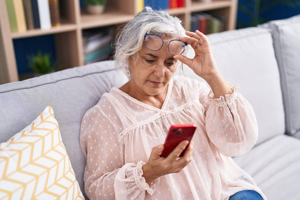 Középkorú ősz hajú nő keres képernyő okostelefon látás probléma otthon - Fotó, kép