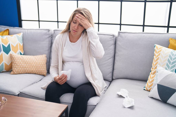 Молода вагітна жінка, яка страждає від головного болю, сидить на дивані вдома
 - Фото, зображення