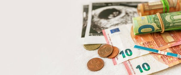 Banner. Schwangerschaftstest, Geld, Banknoten und Ultraschallbild des Babys auf weißem Hintergrund mit Kopierraum. Schwangerschaftsplanung, IVF, Geld für ein Kind, staatliche Zahlungen für ein Kind. - Foto, Bild