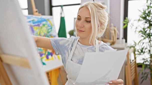 Jovem artista loira confiante sorrindo enquanto desenha em papel no estúdio de arte - Foto, Imagem