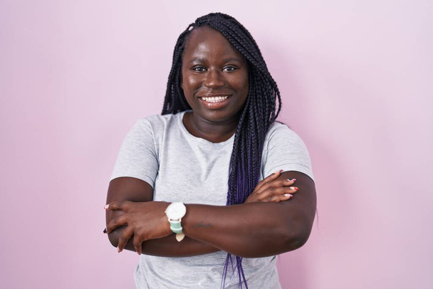 Jeune femme africaine debout sur fond rose heureux visage souriant avec les bras croisés regardant la caméra. personne positive.  - Photo, image