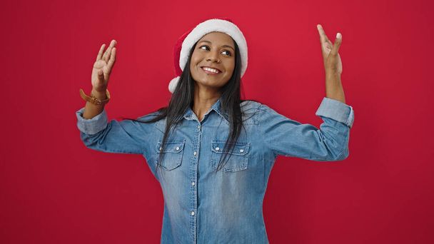 アフリカ系アメリカ人女性,クリスマスの帽子を着て,隔離された赤い背景で踊る - 写真・画像