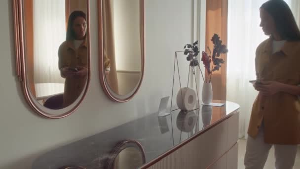 Kaukázusi nő sötét hajjal jön a tükör elé, fényképeket készít a tükörképéről és elsétál. - Felvétel, videó