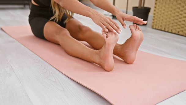 Femme sportive étirant les jambes avec les mains sur le tapis de yoga, mode de vie de la maison d'un athlète en bonne santé séance d'entraînement dans le salon - Photo, image