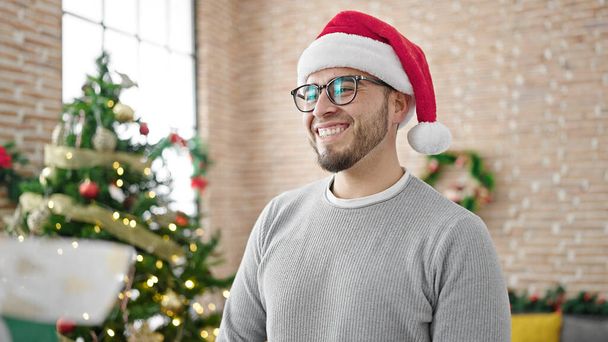 Spanischer Mann lächelt selbstbewusst mit Weihnachtsmütze zu Hause - Foto, Bild