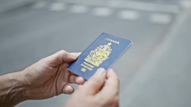 Сіроволоса людина середнього віку, випадково стильно, розкриває свій канадський паспорт, оскільки він патріотично стоїть на сонячній, міській вулиці. - Кадри, відео