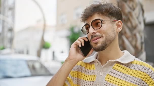 Nuori arabi mies hymyilee luottavainen puhuu älypuhelimeen kadulla - Materiaali, video