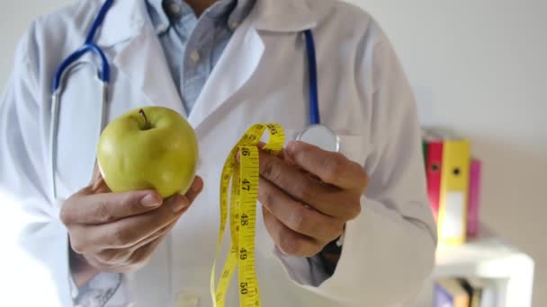 молодой доктор держит яблоко и измерительную ленту  - Кадры, видео