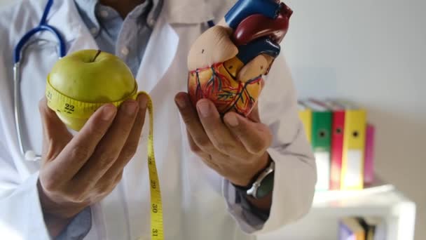 Arzt mit Herzmodell, Apfel und Maßband im Krankenhaus, medizinisches und Gesundheitskonzept - Filmmaterial, Video