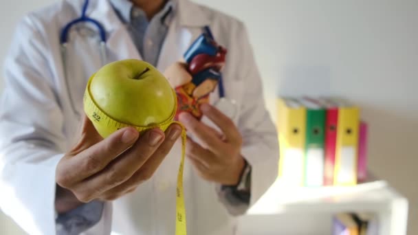 médecin tenant modèle cardiaque, pomme et ruban à mesurer à l'hôpital, concept médical et de soins de santé - Séquence, vidéo