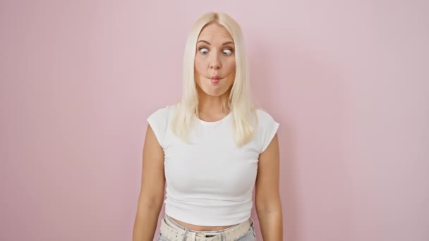 Młoda blondynka, komicznie stojąca nad odosobnionym różowym tłem, robiąca szalony rybi gest twarzy! zabawny, zabawny wyraz twarzy na ustach - Materiał filmowy, wideo