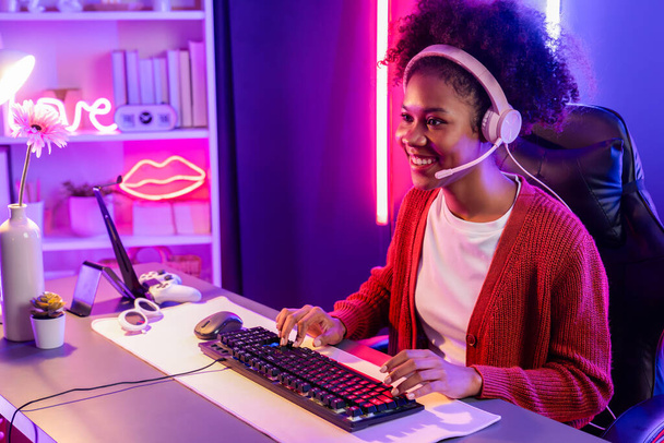 Gaming streamer, African girl playing online fighting with Esport skilled team wearing headphones in neon color lighting room. Talking other players planing strategies to win competitors. Tastemaker. - Photo, Image
