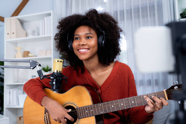 Hostitelský kanál krásné africké ženy ovlivňující zpěv s hrou na kytaru v broadcast studiu na smartphonu. Time slot of music blogger on live social media. Koncept audio tvůrce. Tastemaker. - Fotografie, Obrázek