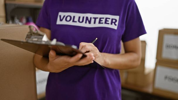 Die fleißigen Hände der hispanischen Freiwilligenhelferin schreiben gewissenhaft Spenden-Checkliste im Wohltätigkeitszentrum - Symbol der altruistischen Unterstützung der Gemeinschaft - Foto, Bild