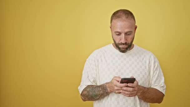 Oszołomiony młody człowiek patrząc bokiem podczas korzystania z telefonu, całkowicie zdumiony wiadomością, odizolowany na żółtym tle - Materiał filmowy, wideo
