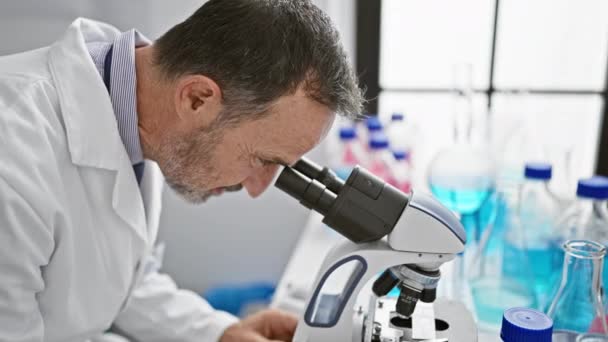 笑顔の中年男性は灰色の髪で,顕微鏡を使って研究室で喜んで科学を受け入れている. - 映像、動画