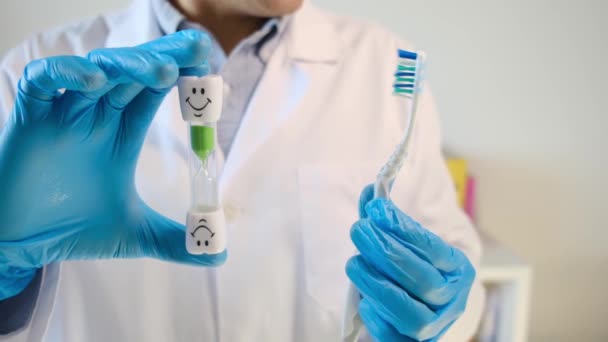 doctor dentista sosteniendo cepillo de dientes y reloj de arena - Imágenes, Vídeo