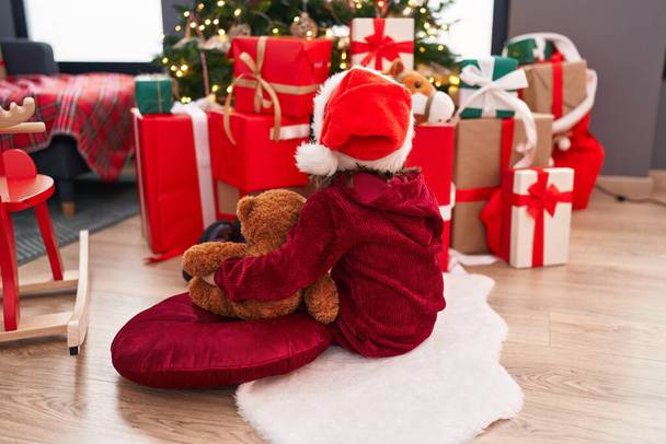 Чарівна іспаномовна дівчина обіймає плюшевого ведмедя, сидячи на дивані різдвяним декором вдома - Фото, зображення