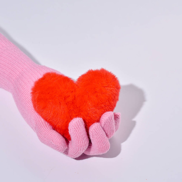 A mão de uma mulher em uma luva de lã segura um coração de pele, a ideia de cuidado, amor, bondade. - Foto, Imagem