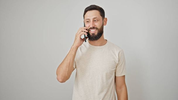 Jonge Spaanse man glimlachend zelfverzekerd praten op de smartphone over geïsoleerde witte achtergrond - Foto, afbeelding